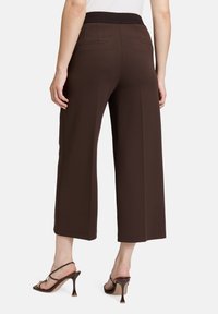 Pantalons larges marron avec une ceinture texturée, dotés de poches arrière. Associés à des sandales à talons hauts avec des lanières.