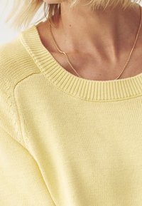 Żółty sweter z dzianiny z rafiową dekoltem, z teksturowanym wzorem na ramionach i luźnym krojem.