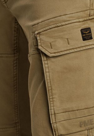 Pantalons cargo beiges en tissu texturé, avec une poche latérale, des détails cousus et une petite étiquette de marque noire.