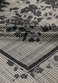 Black and white patterned scarf with floral designs overlaid on a houndstooth base. It features a contrasting border and brand label.