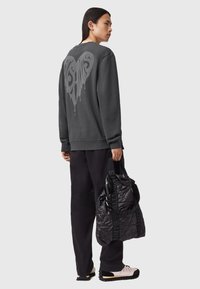 Grå sweatshirt med et stort hjertegrafik på ryggen, parret med sorte bukser og en tekstureret sort taske med en logo-rem.