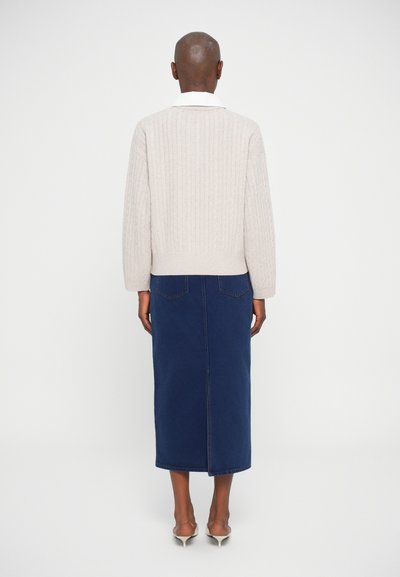 Jasno beżowy sweter z prążkowanej tkaniny, z szerokim kołnierzem, zestawiony z ciemnoniebieską spódnicą midi z denimu. Stylizacja ma prostą sylwetkę i minimalistyczny design.