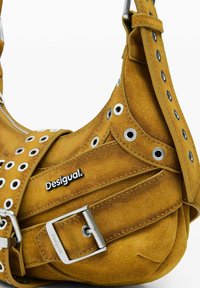 Šuplja žuta suđena torba s srebrnim metalnim rupama, kopčom, patentnim zatvaračem i "Desigual" logom sa strane.