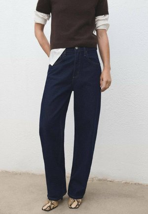 Vaqueros de pierna ancha azul marino con cintura alta, combinados con una blusa de punto de manga corta marrón y zapatos de estampado de serpiente texturizados. Fondo liso.