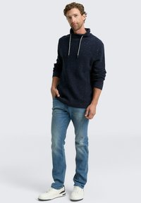 Marineblaues Hoodie mit gesprenkeltem Muster, Kapuze mit Kordelzug, gerippte Bündchen, kombiniert mit hellblauen Jeans und weißen Sneakers. Lässiger Schnitt.