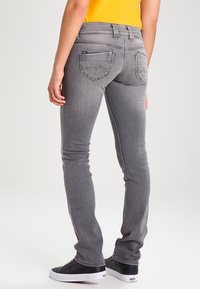 Vaqueros de mezclilla gris con un diseño ajustado, que cuentan con dos bolsillos traseros y un desgaste sutil. Combinados con zapatillas negras y una camiseta amarilla.