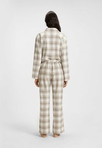 Ruskea ja beige ruudullinen pyjama-asukokonaisuus, jossa on pitkät hihat ja joustava vyötärö, sisältäen rentoa leikkausta ja pehmeää kangastuntumaa.