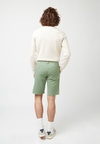 Pantalones cortos verdes con un corte a medida, combinados con un sudadera color crema. Los pantalones cortos cuentan con bolsillos traseros y se llevan con calcetines blancos y zapatillas.