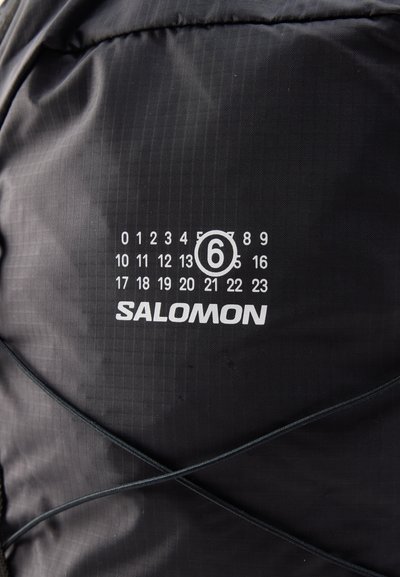 Μαύρο ύφασμα με λευκό αριθμητικό ημερολόγιο που επισημαίνει τον αριθμό 6 και το όνομα της μάρκας Salomon από κάτω.