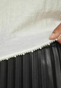 Falda negra plisada con una suave superposición de tela blanca, acentuada por un borde similar a perlas a lo largo del dobladillo, que añade textura y detalle.