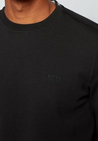 Sudadera negra de algodón con cuello redondeado. Cuenta con un sutil logoembossado en el pecho y detalles en los hombros.