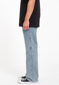Light blue denim jeans with a straight cut, stitched seams, and a slight faded texture, paired with black canvas sneakers.