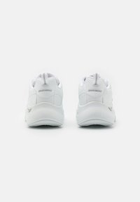 Zapatillas blancas con un upper sintético suave, cuello acolchado y un sutil logo en el talón. Presentan una suela blanca texturizada y una tira de agarre.