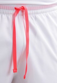 Short blanc avec taille élastique et cordon de serrage corail vif noué, suspendu au centre devant.