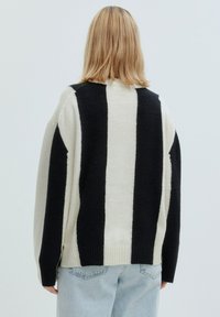 Oversized Pullover in cremfarben mit schwarzen vertikalen Streifen; strukturiertes Strickmaterial; gerippter Saum, Bündchen und lockere Passform; minimalistisches Design.