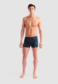 Schwarze Badeshorts mit blauem diagonalen Streifenmuster, aus elastischem Material gefertigt, mit enger Passform und einem Logo auf der Vorderseite.