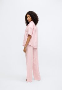 Ριγέ ροζ σετ ρούχων για χαλάρωση που περιλαμβάνει πουκάμισο με κοντά μανίκια και κουμπιά, καθώς και φαρδιά παντελόνια με χαλαρή σιλουέτα.