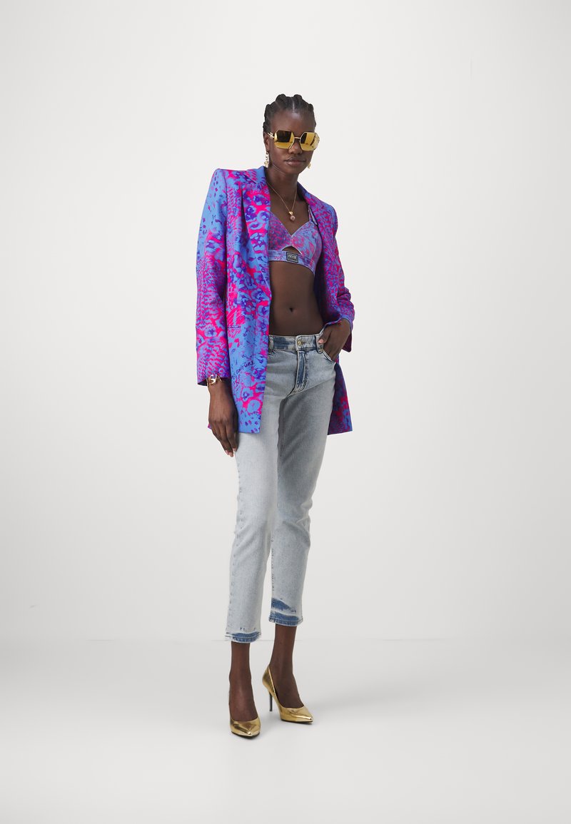Jasnoniebieska i różowa wzorzysta marynarka noszona na lawendowym staniku, w zestawieniu z jasnoniebieskimi dżinsami z przetarciami i złotymi szpilkami. Złote okulary przeciwsłoneczne do kompletu.