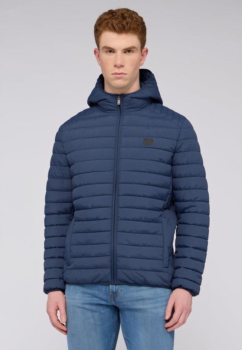 Námořnická puffer bunda se zipem vpředu, horizontálně prošívaným designem, nastavitelnou kapucí a bočními kapsami. Tkanina vypadá hladce se mírným leskem.