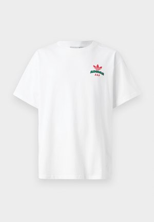 Valkoinen lyhythihainen t-paita, jossa pieni punainen ja vihreä Adidas-logo vasemmalla ylärintakehällä.