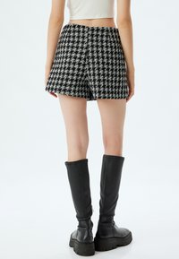 Pantalones cortos a cuadros en blanco y negro, con textura tejida y diseño de cintura alta. Combinados con botas negras de cuero hasta la rodilla y una camiseta corta.