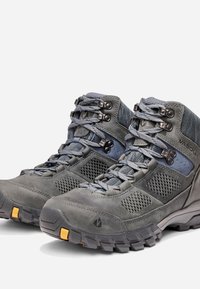Botas de senderismo grises con paneles de malla, cuero texturizado y ojetes de metal. Presentan suelas robustas con acentos amarillos para mayor tracción.