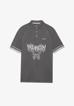 Polo gris avec un graphisme de papillon en blanc et le mot "PRDMN" au-dessus. Le col a une patte de boutonnage à trois boutons et des manches rayées.