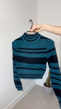 Pulover scurt, cu dungi albastre și negre, cu guler înalt și mâneci lungi, fabricat dintr-un material tricotat cu nervuri. Include umeraș.