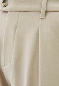 Beige op maat gemaakte broeken met een soepele textuur, voorzien van een geplooide voorkant, zijzakken en een knoopsluiting bij de taille.