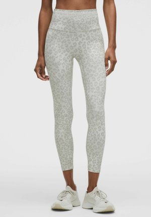 Legginsy slim fit z wysokim stanem w jasnoszary i biały print lamparta, noszone przez stojącą osobę w białych butach sportowych.