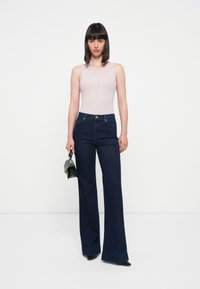 Un top fără mâneci de culoare roz pal, blugi evazați de culoare albastru închis și accesorii negre. Blugii au talie înaltă și buzunare frontale.
