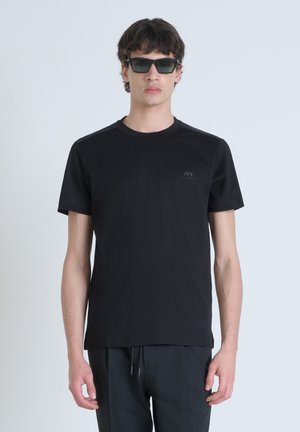 Camiseta de algodón negra con cuello redondo, mangas cortas y un pequeño logo en el pecho, combinada con gafas de sol oscuras.