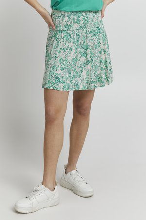 Grøn mini-nederdel med blomsterprint og smock-talje. Lavet af letvægtsstof. Kombinationet med hvide sneakers giver et afslappet look.