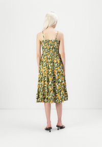 Robe d'été en coton avec un motif floral vert présentant des fruits jaunes. Corsage ajusté avec fronces et jupe évasée. Fines bretelles.