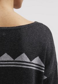 Pull noir avec un col large, présentant un motif géométrique gris et des rayures horizontales dans le haut du dos. Texture douce.