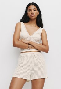 Crème-kleurige gebreide loungewear set met een mouwloze top met diepe V-hals en shorts met trekkoord, voorzien van verticale geribbelde textuur en accentrandjes.