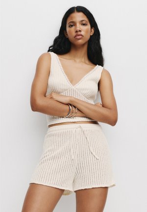 Crème-kleurige gebreide loungewear set met een mouwloze top met diepe V-hals en shorts met trekkoord, voorzien van verticale geribbelde textuur en accentrandjes.