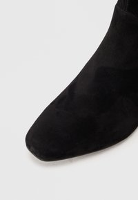 Svart mocka ankelboot med spetsig tå och slät yta, med en smal klack och minimalistisk design.
