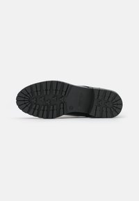 Sole in gomma nera con profonde scanalature e superficie texturizzata, dotata di dettagli di branding e un design robusto e resistente.