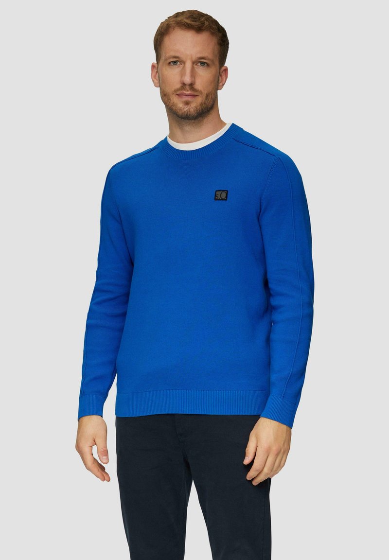 Blauwe gebreide trui met een ronde halslijn, geribbelde manchetten en zoom. Heeft een zwart logo-label op de borst. Glad textuur, aansluitend ontwerp.