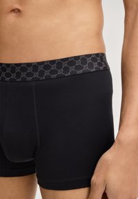 Mustat boxerit, joissa on kuvioitu harmaa vyötärönauha. Valmistettu sileästä kankaasta, tiukka istuvuus ja litteät saumat mukavuutta varten.