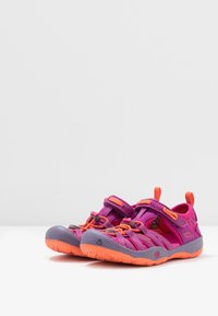 Zapatos abiertos de dedo en morado y rosa con acentos en naranja, que cuentan con correas ajustables y suelas de goma texturizadas para mayor agarre. Diseño ligero.
