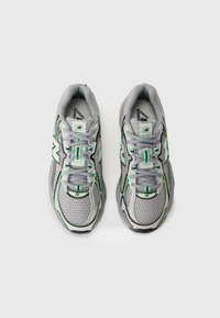 Baskets de sport grises avec une tige en maille, dotées d'accents verts et de finitions noires. Conçues avec des semelles rembourrées et un laçage traditionnel.