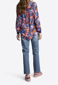 Camicia a maniche lunghe colorata e a fantasia nei toni del rosa, blu e arancione, abbinata a jeans azzurri e sandali rosa.