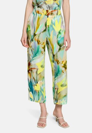 Loose-fitting pants with multicolored abstract floral pattern in greens, yellows, and blues, worn with beige heeled sandals.