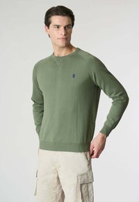 Maglione verde lavorato a maglia con scollatura rotonda e polsini a costine. Presenta un piccolo logo blu sul petto e un design a vestibilità rilassata.