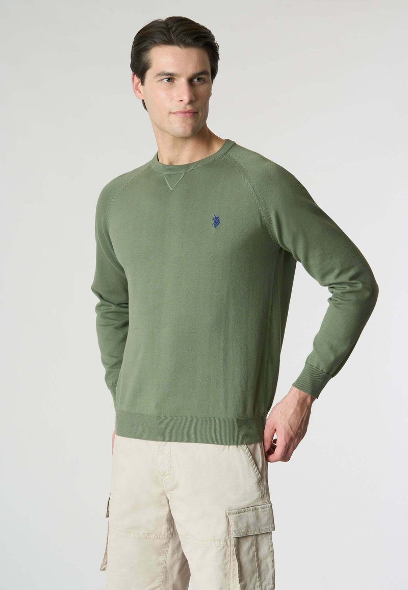 Maglione verde lavorato a maglia con scollatura rotonda e polsini a costine. Presenta un piccolo logo blu sul petto e un design a vestibilità rilassata.