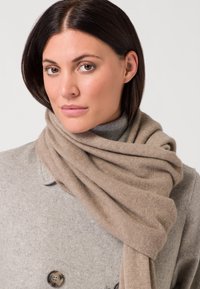 Sciarpa di lana beige appoggiata su un cappotto grigio, caratterizzata da una texture morbida e da una vestibilità ampia intorno al collo, che aumenta calore e comfort.