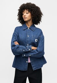 Μπλε σκουρό τζιν μπουφάν με μακριά μανίκια, κλείσιμο με κουμπιά και τσέπη στο στήθος. Διαθέτει ετικέτα με λογότυπο στην τσέπη και ελαφρώς φαρδιά εφαρμογή.