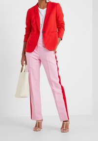 Punainen bleiseri valkoisen t-paidan päällä, yhdistettynä vaaleanpunaisiin housuihin, joissa on punaiset sivunauhat. Kevyt kangas, suoralahkeinen muotoilu ja avonaiset korkokengät.